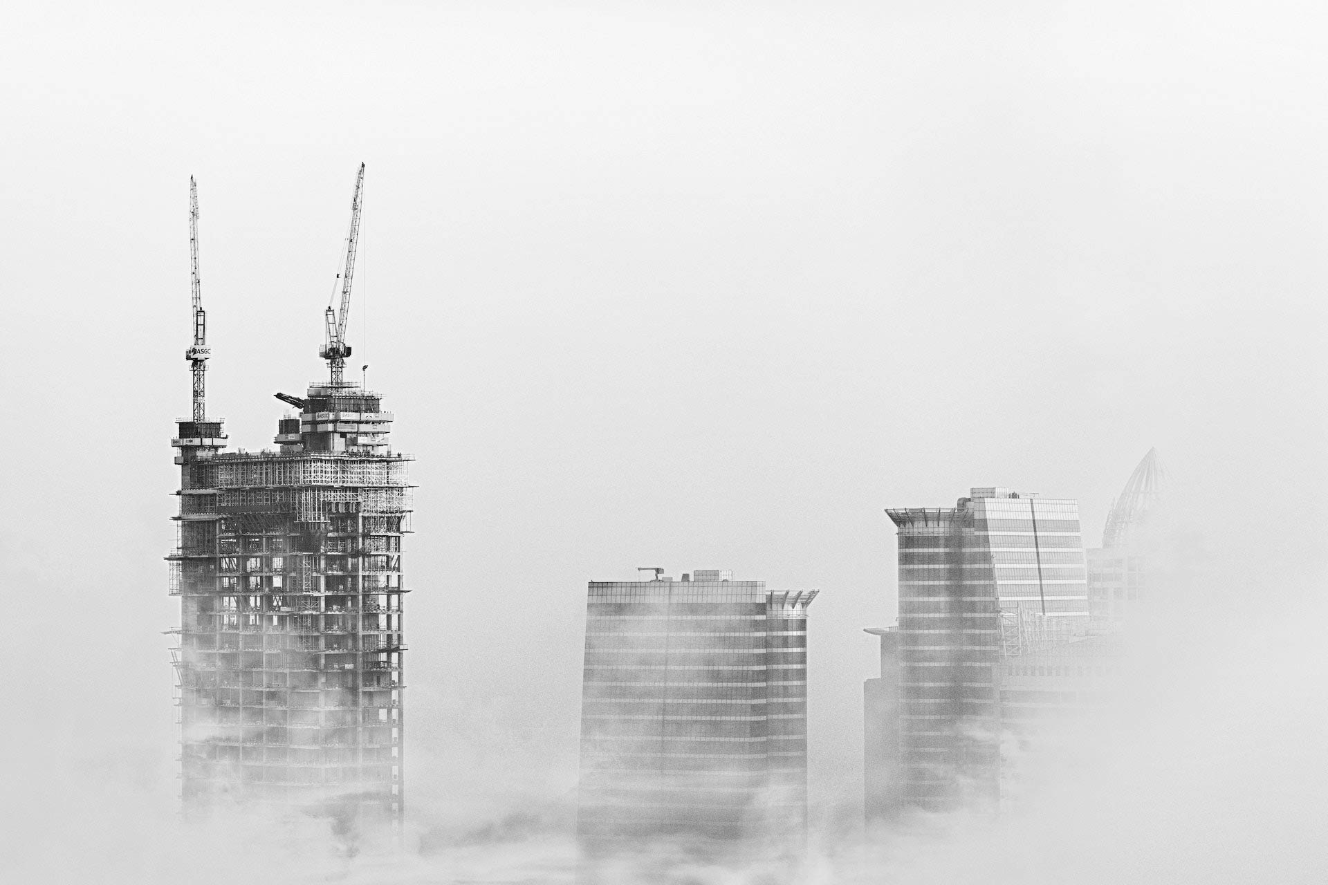 Construction tower rising through fog beside city buildings